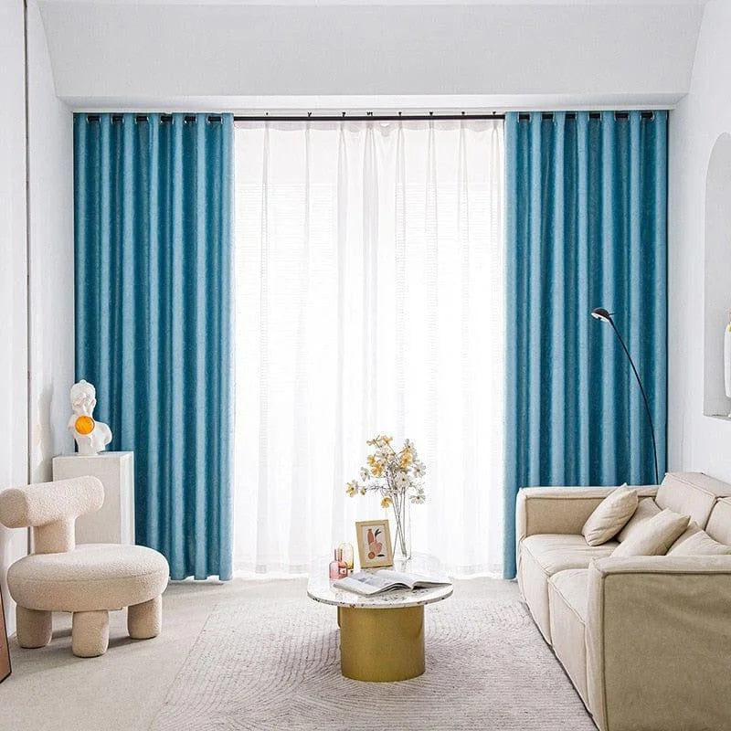 Salon moderne avec canapé beige, rideaux bleu turquoise et voilage blanc, fauteuil design et table basse circulaire dorée. Ambiance lumineuse et épurée, idéale pour un style contemporain et élégant.