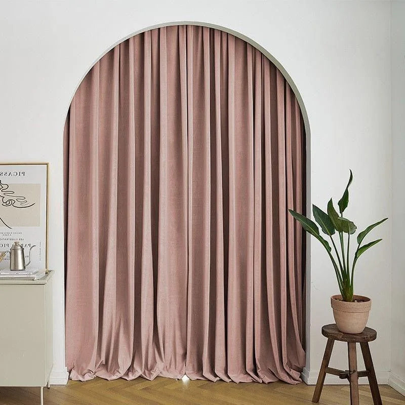 Rideau élégant rose dans un salon moderne. Ce rideau long ajoute une touche sophistiquée à l'intérieur avec son design arqué unique. Idéal pour apporter une ambiance chaleureuse et intimiste à votre espace. Le sol en bois clair et la plante d'intérieur complètent parfaitement le décor accueillant.