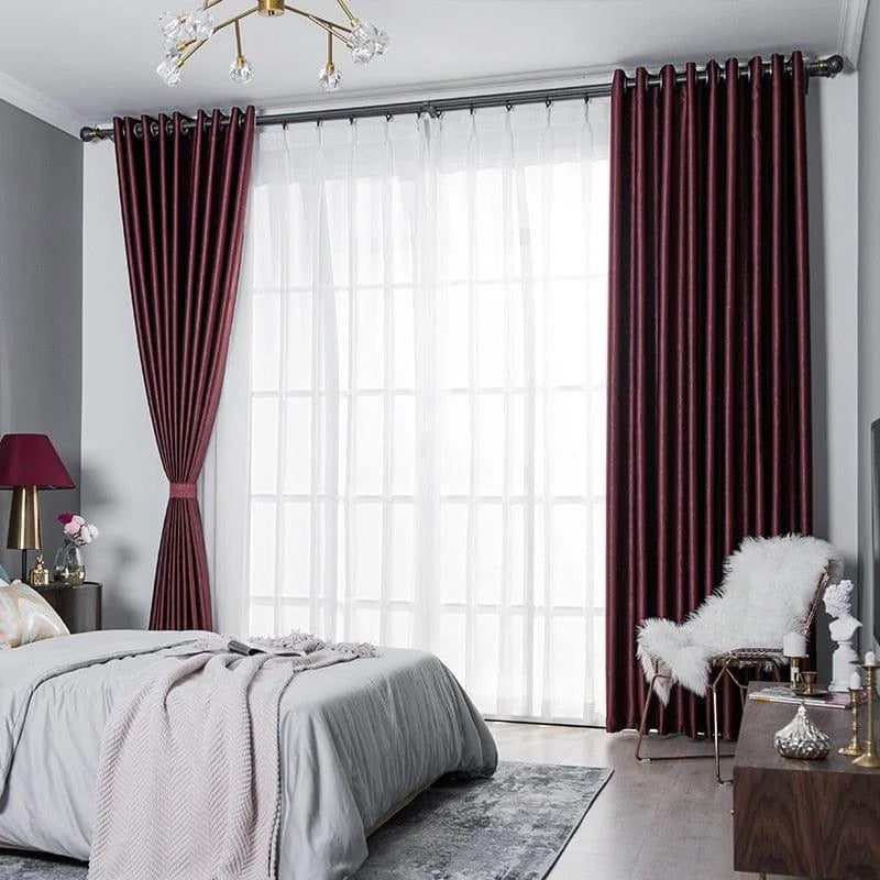 Chambre élégante avec rideaux bordeaux et voilages blancs, offrant un style moderne et raffiné. Lit confortable avec une lampe de chevet assortie et un tapis discret créant une ambiance chaleureuse. Meubles design en bois et chaise avec coussin en fausse fourrure ajoutant une touche de luxe à la décoration intérieure. Lustre contemporain illuminant la pièce pour un éclairage optimal. Idéal pour les amateurs de décoration sophistiquée et tendance.