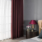 Rideaux élégants en teinte pourpre offrant une ambiance chaleureuse et sophistiquée à la chambre. Contraste moderne avec le mur gris et la décoration soignée d'une table de chevet avec lampe et fleurs, idéal pour sublimer votre intérieur.