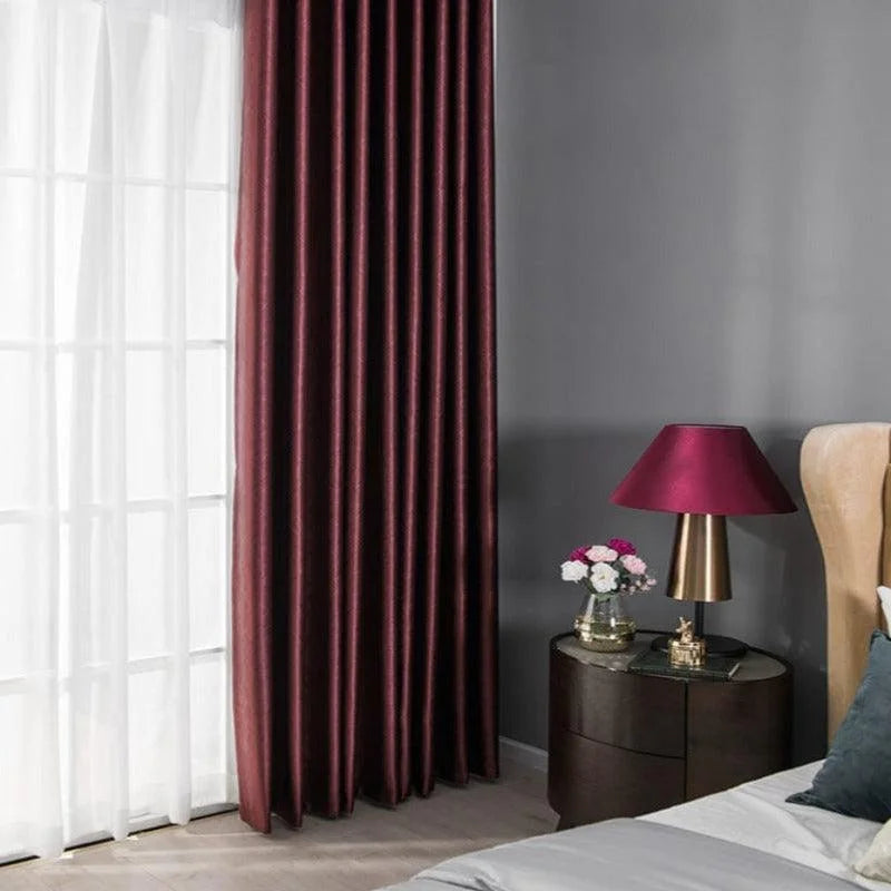 Rideaux élégants en teinte pourpre offrant une ambiance chaleureuse et sophistiquée à la chambre. Contraste moderne avec le mur gris et la décoration soignée d'une table de chevet avec lampe et fleurs, idéal pour sublimer votre intérieur.