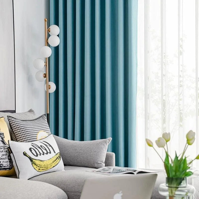 Rideaux bleu élégants dans un salon moderne, rehaussant le décor contemporain avec des coussins décoratifs colorés sur un canapé gris confortable, une lampe design et un vase de fleurs ajoutant une touche de fraîcheur. Idéal pour créer une atmosphère chaleureuse et accueillante.