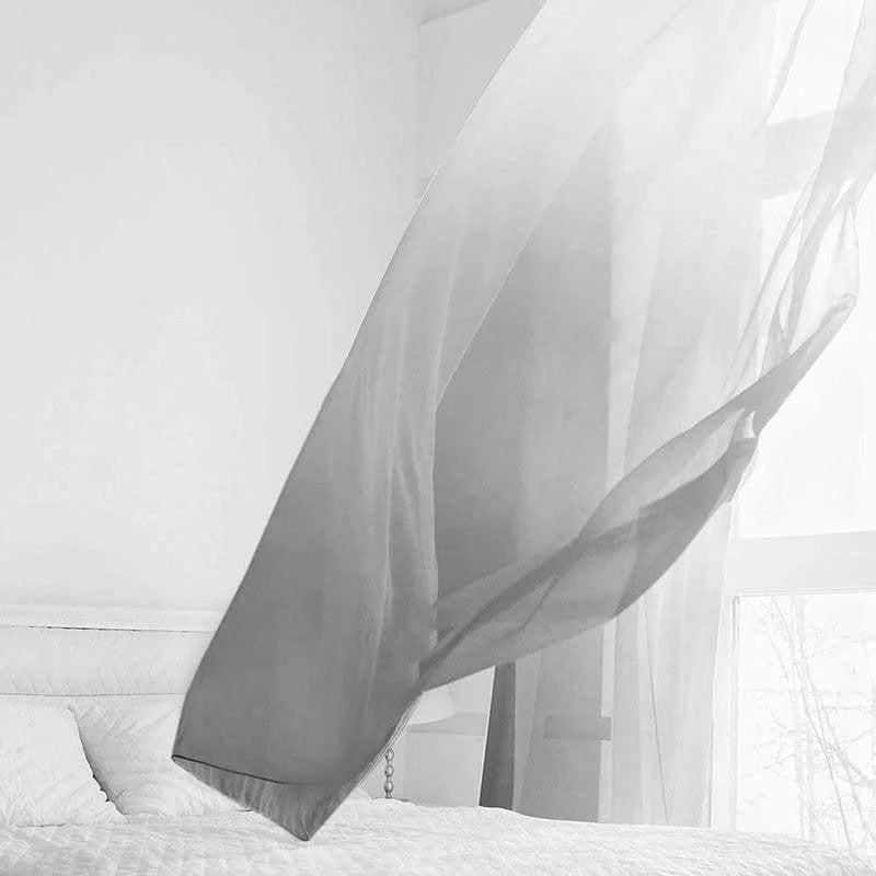 Voilage transparent flottant dans une chambre minimaliste avec un éclairage naturel provenant d'une grande fenêtre, ambiance apaisante et lumineuse propice à la relaxation.