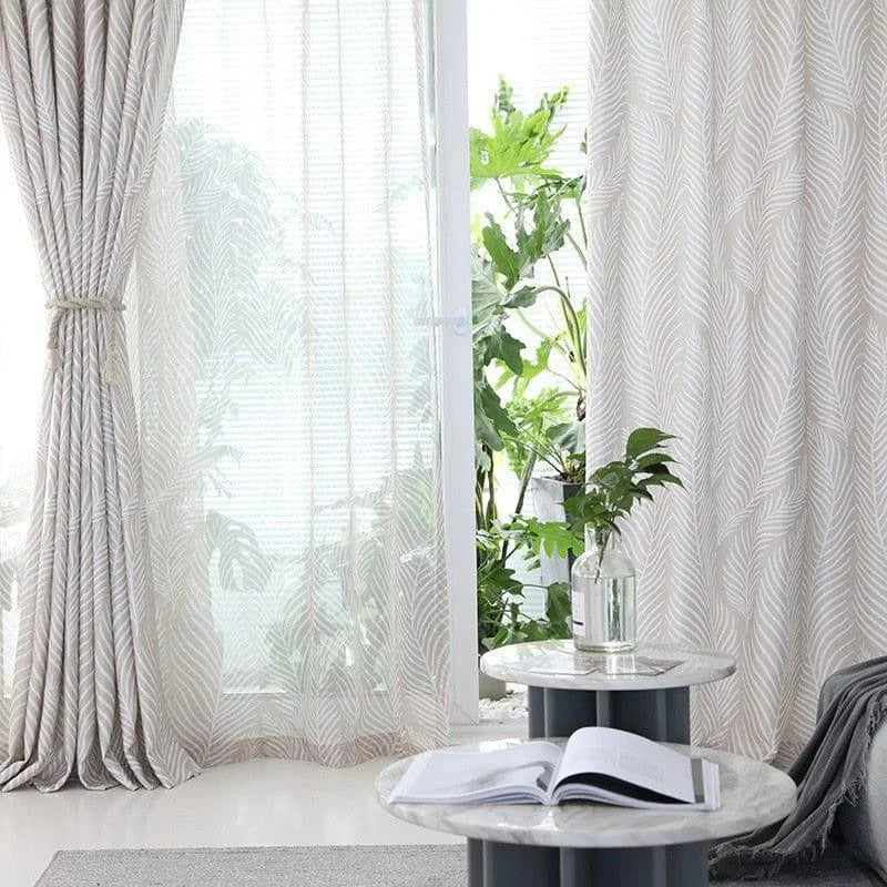 Rideaux à motifs de feuilles blanches devant une fenêtre, apportant une ambiance lumineuse et moderne à votre salon. Ces rideaux élégants filtrent délicatement la lumière du jour tout en préservant votre intimité. Idéal pour créer un cadre apaisant et naturel, accentué par des plantes vertes et une décoration intérieure raffinée. Parfait pour embellir tout type d'espace avec style et sophistication.