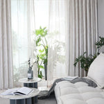 Salon moderne avec rideaux élégants et plantes vertes, mettant en valeur une ambiance lumineuse et naturelle. Les tables basses rondes apportent une touche contemporaine, offrant un espace accueillant pour la détente et la lecture.
