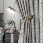 Rideaux modernes avec motif foliaire, ajoutant une touche élégante à la décoration intérieure d'une chambre contemporaine. L'agencement avec une embrasse dorée souligne le style raffiné tout en permettant de moduler la luminosité selon les envies. Parfaits pour apporter du cachet à votre espace de vie.