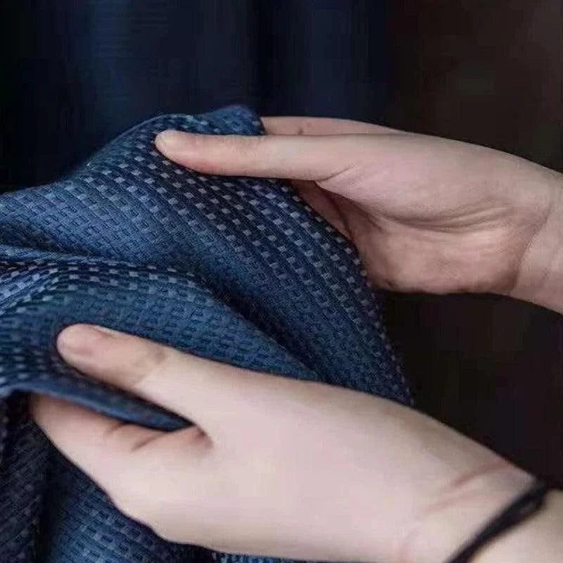 Deux mains tiennent un tissu bleu texturé avec un motif en damier. Cette étoffe, soigneusement examinée, met en valeur son style élégant et son design moderne. Parfait pour une utilisation dans la décoration intérieure ou la confection de vêtements sophistiqués.