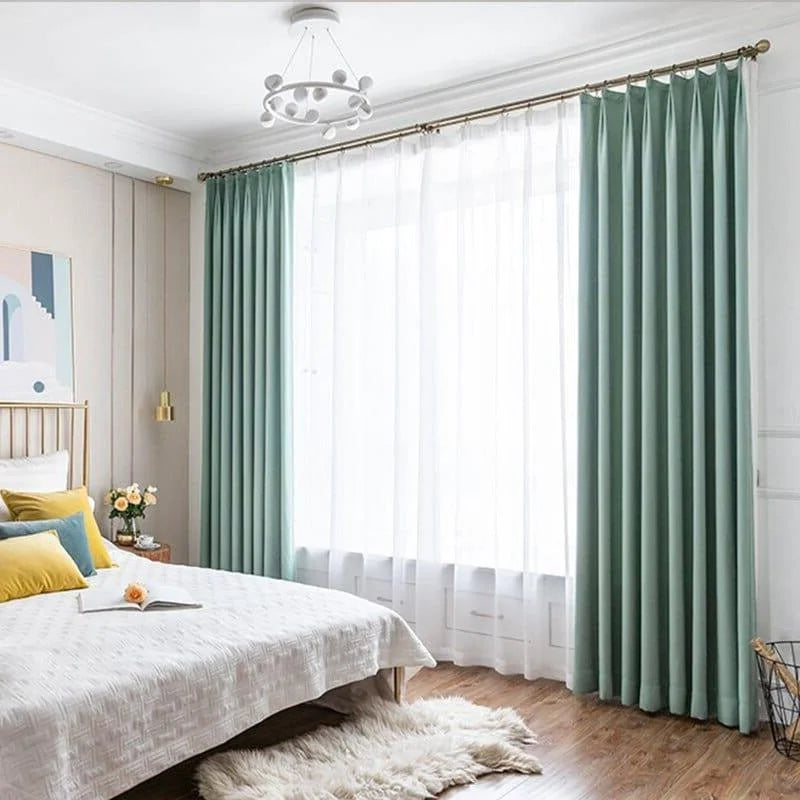 Chambre moderne avec rideaux verts, lit confortable avec coussins colorés, et parquet élégant. Éclairage doux et décor harmonieux pour un intérieur apaisant. Design contemporain et tendance pour une ambiance relaxante.