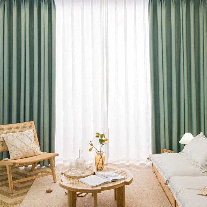 Salon moderne avec décor minimaliste. Rideaux verts et blancs en arrière-plan, meubles en bois clair, fauteuil et canapé confortables. Table basse avec vase et livres, ambiance lumineuse et apaisante idéale pour la détente et la lecture.
