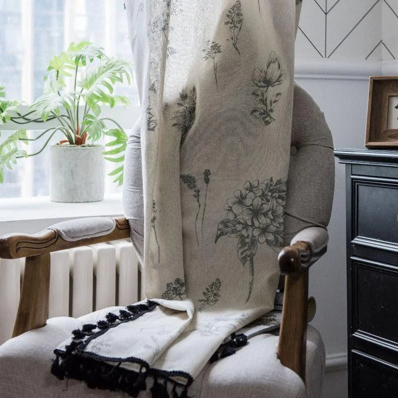 Rideau décoratif avec motifs floraux élégamment suspendu sur une chaise dans un intérieur lumineux. Idéal pour apporter une touche de nature et de style à votre salon ou chambre. À côté, une plante verte ajoute une ambiance naturelle apaisante. Parfait pour ceux qui cherchent à enrichir leur décoration intérieure avec des accents sophistiqués et chaleureux.