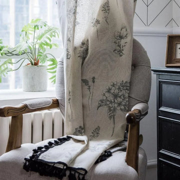 Rideau décoratif avec motifs floraux élégamment suspendu sur une chaise dans un intérieur lumineux. Idéal pour apporter une touche de nature et de style à votre salon ou chambre. À côté, une plante verte ajoute une ambiance naturelle apaisante. Parfait pour ceux qui cherchent à enrichir leur décoration intérieure avec des accents sophistiqués et chaleureux.
