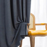 Rideau élégant de couleur sombre, harmonieusement drapé à côté d'une chaise de style classique avec assise jaune vif. Idéal pour apporter une touche sophistiquée à votre salon ou chambre à coucher, le rideau assure une décoration intérieure moderne et chic.