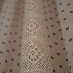 Motifs délicats de dentelle et petites fleurs sur fond beige, parfaits pour une décoration intérieure élégante. Ce tissu aux motifs raffinés apporte une touche de charme vintage à votre espace de vie. Idéal pour rideaux, nappes ou projets créatifs, il se distingue par son design subtil et son allure chic.