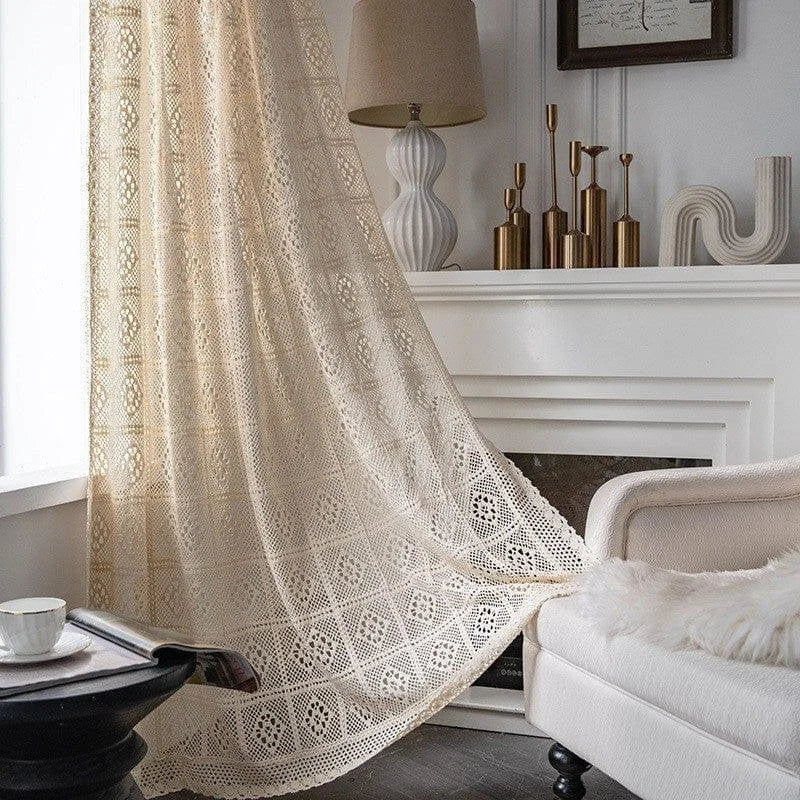 Voilage élégant beige aux motifs géométriques suspendu dans un salon moderne. Ce rideau décoratif ajoute une touche de sophistication à l'intérieur, complétant harmonieusement le mobilier épuré et les accessoires en métal doré sur la cheminée. Idéal pour créer une ambiance chaleureuse et accueillante.