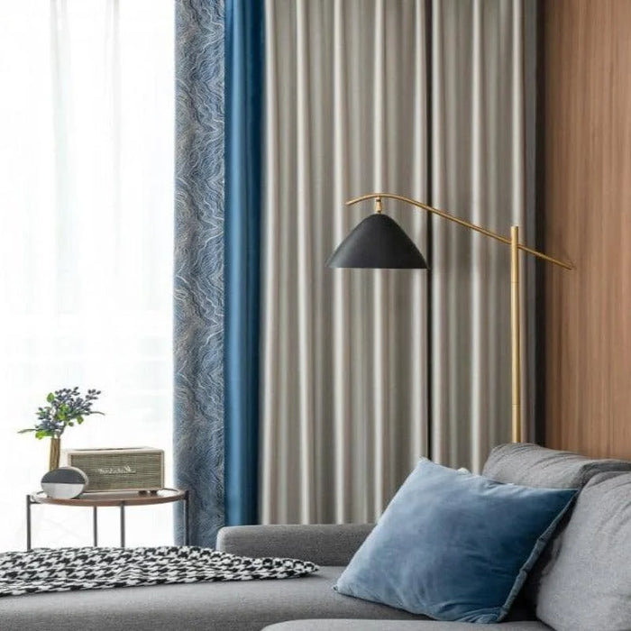 Salon chic et moderne avec canapé gris orné d'un coussin bleu, table d'appoint élégante, rideaux élégants, et lampadaire design. Ambiance chaleureuse et accueillante idéale pour la décoration intérieure contemporaine.