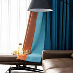 Rideaux modernes aux teintes bleu et orange, ornant un intérieur élégant. L'ambiance chic est accentuée par un canapé confortable et une table d'appoint avec des verres et une carafe, parfaite pour un salon contemporain.