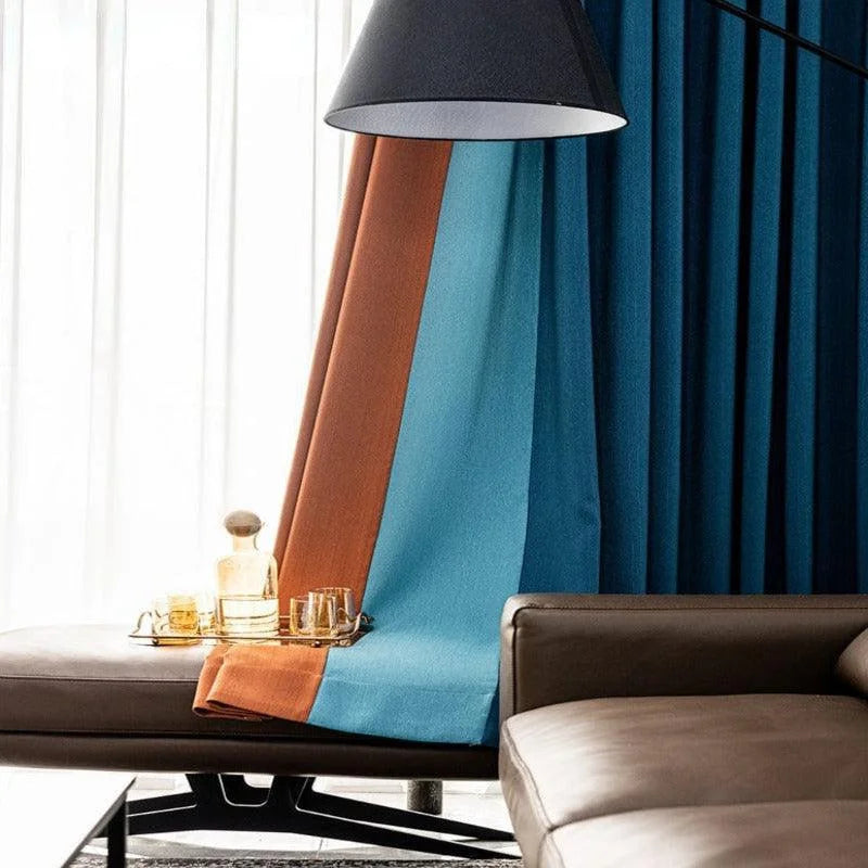Rideaux modernes aux teintes bleu et orange, ornant un intérieur élégant. L'ambiance chic est accentuée par un canapé confortable et une table d'appoint avec des verres et une carafe, parfaite pour un salon contemporain.