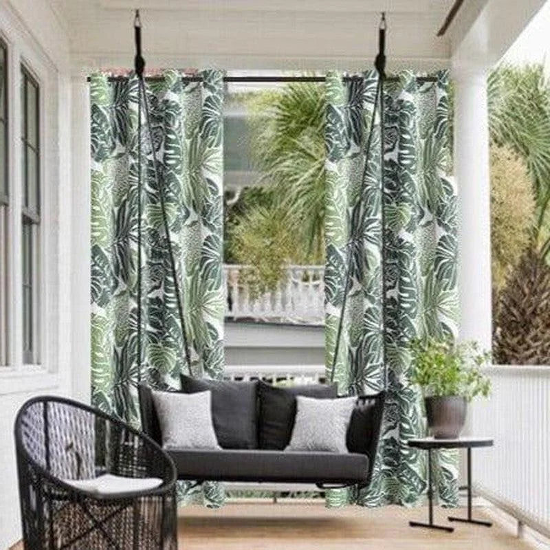 Balancelle extérieure élégante sur une terrasse, idéale pour un moment de détente en plein air. Cette balancelle suspendue est entourée de rideaux à motifs tropicaux, créant un espace cosy et intime. Le mobilier de jardin est complété par une table d'appoint moderne et des coussins confortables, parfaits pour l'été. Cette installation s'intègre harmonieusement dans un environnement verdoyant, offrant une ambiance relaxante et naturelle.