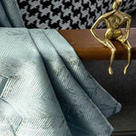 Tissu d'ameublement bleu avec motif géométrique en chevrons, idéal pour la décoration intérieure moderne. Sophistication et élégance s'associent pour embellir votre espace de vie. Accompagné d'une sculpture métallique dorée, ajoutant une touche artistique et contemporaine. Parfait pour personnaliser votre intérieur avec style.