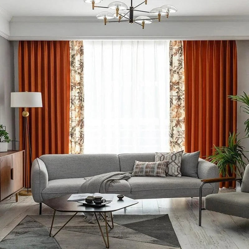 Salon moderne avec décoration élégante, comprenant un canapé gris accueillant et un ensemble de rideaux rouge et motif floral. Éclairage naturel amélioré par une grande fenêtre, complété par une table basse design et des accessoires décoratifs modernes, créant une ambiance chaleureuse et stylée.