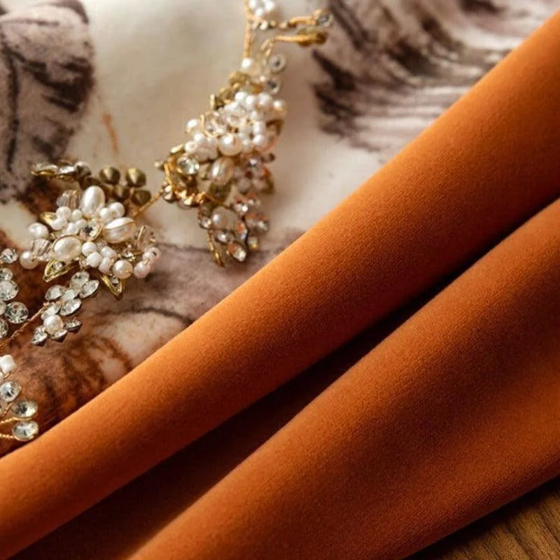Plan rapproché d'un tissu orange élégant accompagné d'un bijou délicat orné de perles et de cristaux. Accessoire raffiné pour ajout de luxe et de sophistication à toute tenue. Idéal pour la décoration intérieure et la couture haut de gamme.