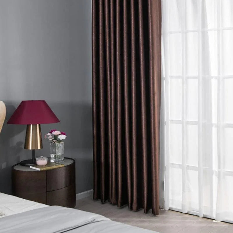 Rideaux opaques marron foncé élégants dans une chambre moderne avec une lumière douce, accompagnés d'un abat-jour rouge et d'une table de chevet en bois, créant une ambiance chaleureuse et accueillante.