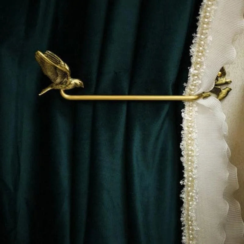 Attache-rideau élégant de couleur dorée avec motif oiseau, tenant des rideaux sombres avec un bord décoratif perlé blanc, idéal pour rehausser la décoration intérieure avec une touche sophistiquée.