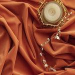 Bougie décorative dorée sur fond orange élégant avec accessoire perlé et feuillages dorés, idéale pour une ambiance chaleureuse et sophistiquée. Décoration intérieure chic, parfait pour les occasions spéciales.