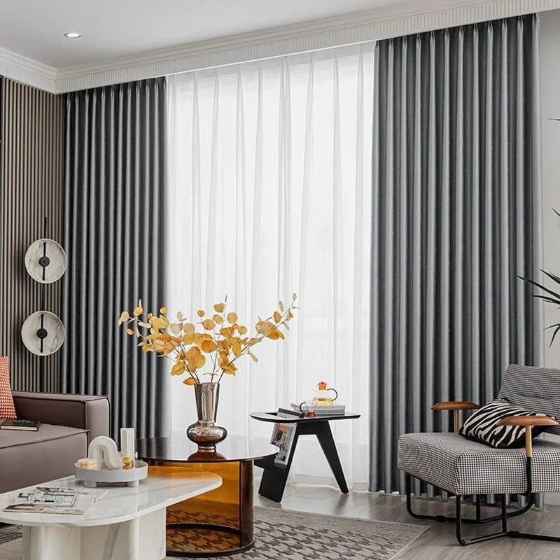 Rideaux occultants gris élégants dans un salon moderne. L'espace est décoré avec des meubles contemporains, comprenant un canapé confortable, une table basse chic, un fauteuil design et une décoration murale artistique. Luminosité douce grâce aux rideaux et à la lumière naturelle, créant une ambiance chaleureuse et accueillante. Parfait pour ajouter une touche de style et d'élégance à votre intérieur.