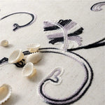 Détail artistique d'un design floral brodé sur un tissu clair, accompagné de coquillages délicats. Cette image met en avant l'élégance et le style d'un motif décoratif sophistiqué, idéal pour la décoration intérieure. Le contraste des couleurs entre les motifs et le fond ajoute une touche de raffinée, parfaite pour embellir n'importe quel espace de vie.