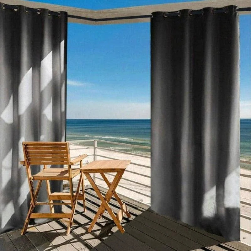 Rideaux d'extérieur foncés suspendus sur une terrasse moderne offrant une vue panoramique sur la mer. Ensemble de mobilier de jardin en bois composé d'une chaise et d'une table pliante, parfait pour se détendre face à l'océan. Idéal pour créer un espace de détente en plein air avec une touche d'élégance.