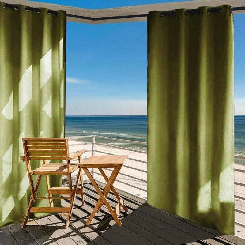 Rideaux occultants verts suspendus sur une terrasse avec vue sur la mer, apportant une touche d'élégance et de confort à l'espace extérieur. Ensemble avec une table et une chaise en bois, idéal pour profiter de la vue panoramique sur l'océan. Solution idéale pour bloquer la lumière tout en ajoutant du style à votre balcon.