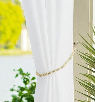 Rideau blanc élégant drapé avec embrasse torsadée, encadrant une fenêtre lumineuse avec vue sur le jardin. Accessoire de décoration intérieure moderne offrant une ambiance lumineuse et rafraîchissante.