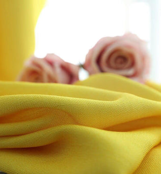 Tissu jaune vif, élégant et doux, parfait pour la décoration intérieure ou la confection de vêtements. Mettez en valeur votre espace avec cette teinte lumineuse et ajoutez une touche de chaleur et de style. Au second plan, des roses pastel ajoutent une touche florale et romantique à l'image.