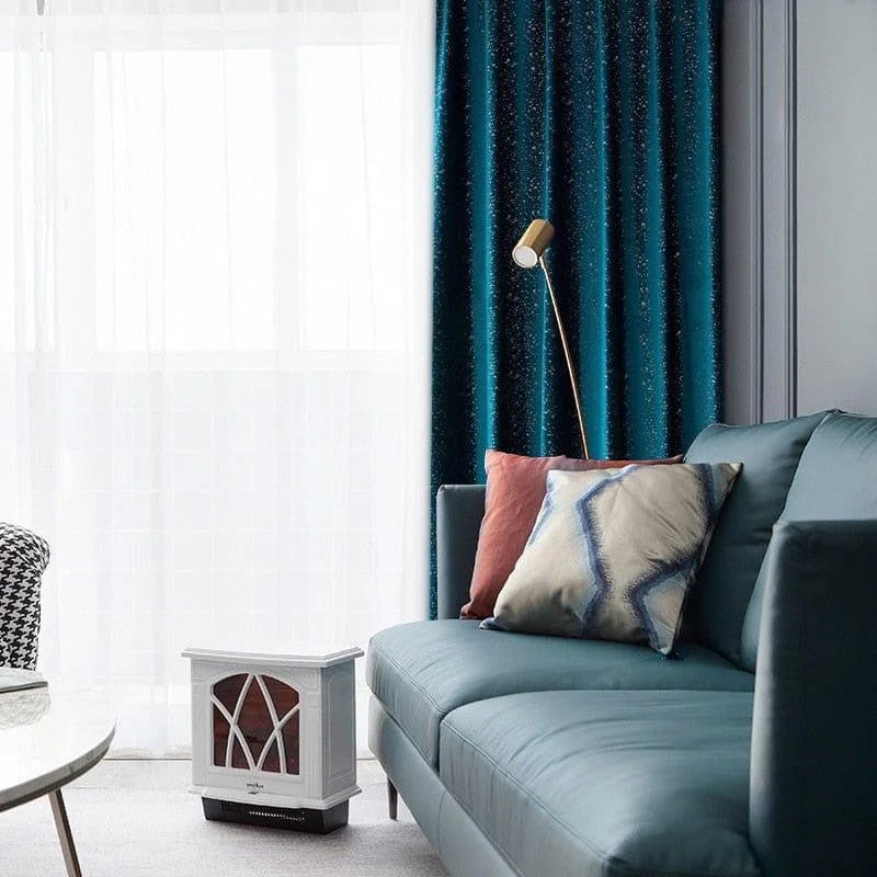 Salon moderne avec un canapé bleu élégant, agrémenté de coussins décoratifs colorés, offrant un confort optimal. Un poêle électrique blanc apporte une touche de chaleur et de style classique à l'espace. Les rideaux bleu foncé ajoutent une note sophistiquée à la pièce, tandis qu'une lampe design dorée complète l'ambiance contemporaine et accueillante.