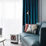 Salon moderne avec un canapé bleu élégant, agrémenté de coussins décoratifs colorés, offrant un confort optimal. Un poêle électrique blanc apporte une touche de chaleur et de style classique à l'espace. Les rideaux bleu foncé ajoutent une note sophistiquée à la pièce, tandis qu'une lampe design dorée complète l'ambiance contemporaine et accueillante.
