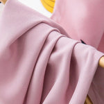 Étoffe rose élégante suspendue à un support, idéale pour confectionner des vêtements modernes et raffinés. Tissu fluide et doux, parfait pour apporter une touche de sophistication à votre garde-robe. Belle texture et couleur délicate, un choix parfait pour des créations tendance.