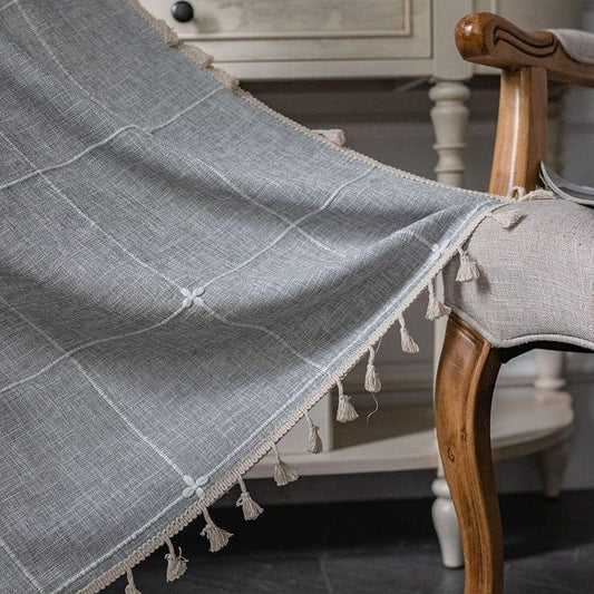 Couverture élégante de couleur grise avec motifs géométriques et franges décoratives, drapée sur un fauteuil en bois. Accessoire idéal pour ajouter une touche de sophistication et de confort à votre intérieur.