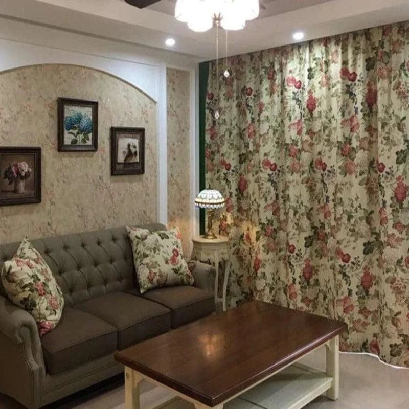 Salon élégant avec canapé capitonné et rideaux floraux, ambiance cosy et décoration vintage, idéal pour une maison au style classique. Tableau floral sur le mur, table basse en bois, et lampe rétro sur une table d'appoint créent un espace accueillant et chaleureux.