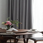 Table à manger élégante avec décoration florale et chaises modernes en bois, située près d'un rideau gris chic. Cette salle à manger raffinée crée une ambiance conviviale et chaleureuse idéale pour les repas en famille ou entre amis, ajoutant une touche de sophistication à votre intérieur.