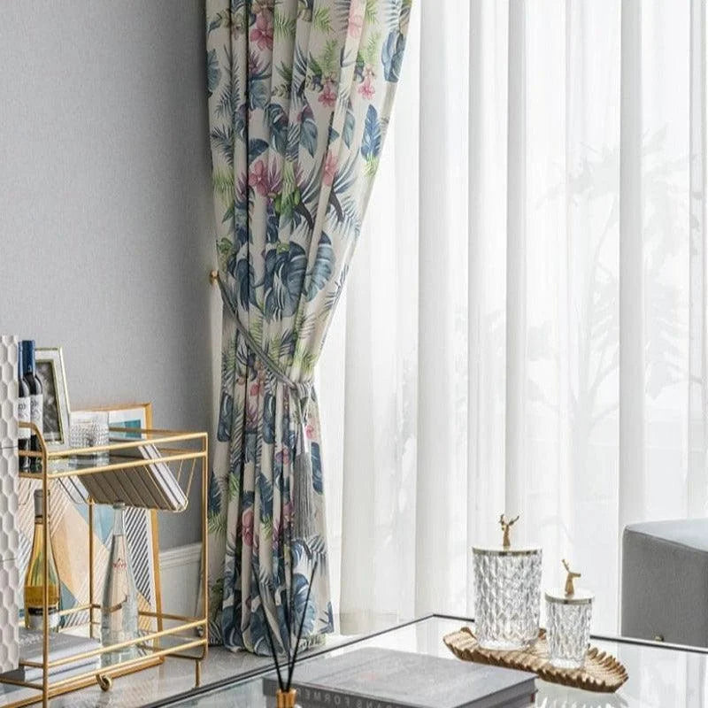 Rideaux imprimés fleuris avec motifs tropicaux, ajoutant une touche élégante et rafraîchissante au salon moderne. Design chic parfait pour illuminer les espaces de vie contemporains avec une décoration intérieure harmonieuse. Accessoires dorés et table basse en verre complètent l'ambiance raffinée.