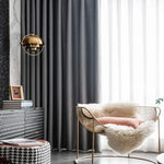 Fauteuil élégant au design moderne, idéal pour salon contemporain. Décoration intérieure avec rideaux sombres contrastés par des voilages blancs, lampe suspendue dorée, et éléments décoratifs tendance. Atmosphère chic et confortable, adaptée pour un coin lecture ou relaxation.