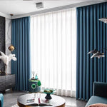 Rideaux élégants bleu foncé pour salon moderne, rehaussant la décoration intérieure avec style contemporain. Fenêtre généreusement éclairée par la lumière naturelle, créant une ambiance accueillante. Accessoires de décoration chic incluant une lampe dorée et des éléments décoratifs verts sur une table basse. Ensemble harmonieux et design pour une pièce à vivre sophistiquée.