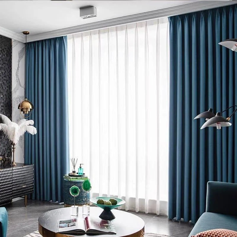 Rideaux élégants bleu foncé pour salon moderne, rehaussant la décoration intérieure avec style contemporain. Fenêtre généreusement éclairée par la lumière naturelle, créant une ambiance accueillante. Accessoires de décoration chic incluant une lampe dorée et des éléments décoratifs verts sur une table basse. Ensemble harmonieux et design pour une pièce à vivre sophistiquée.