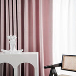 Rideaux élégants rose doux, ajoutant une touche de sophistication à votre intérieur. Statue minimaliste blanche sur une table moderne avec une chaise design à accoudoirs en bois foncé et assise en cannage. Idéal pour un salon chic et contemporain.