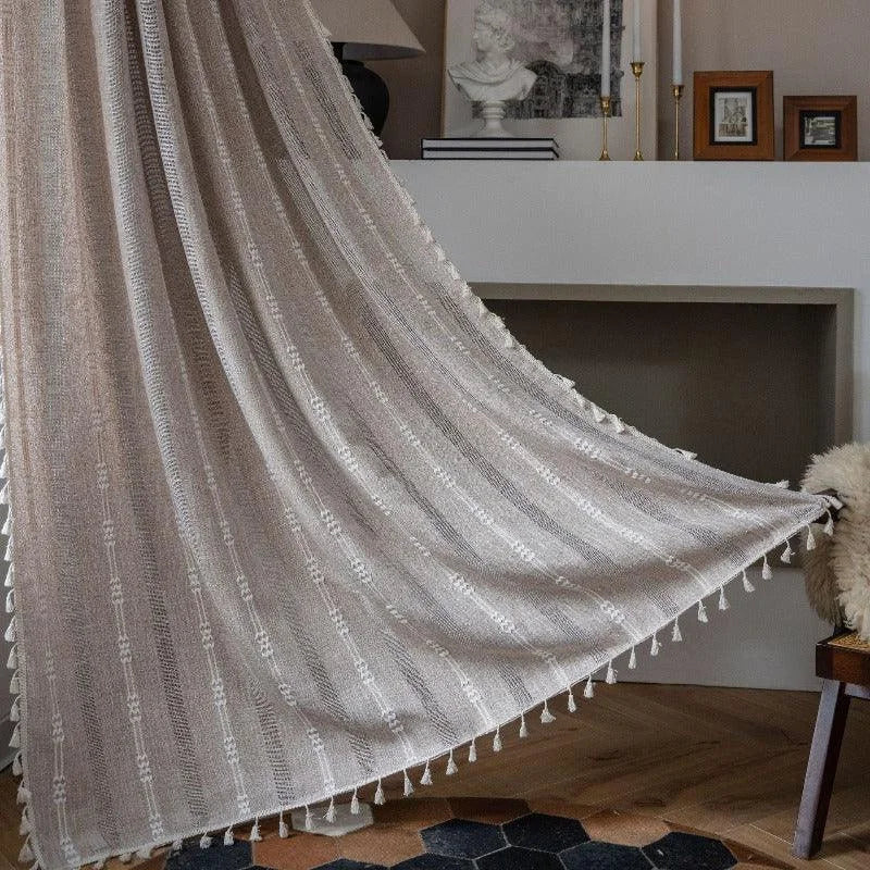 Rideau élégant beige avec motifs verticaux et détails à pompons, installé dans un intérieur moderne et sobre. Décoration raffinée, idéale pour apporter une touche chaleureuse et accueillante à votre salon ou chambre. Accessoire de maison qui combine style et fonctionnalité pour un espace convivial.