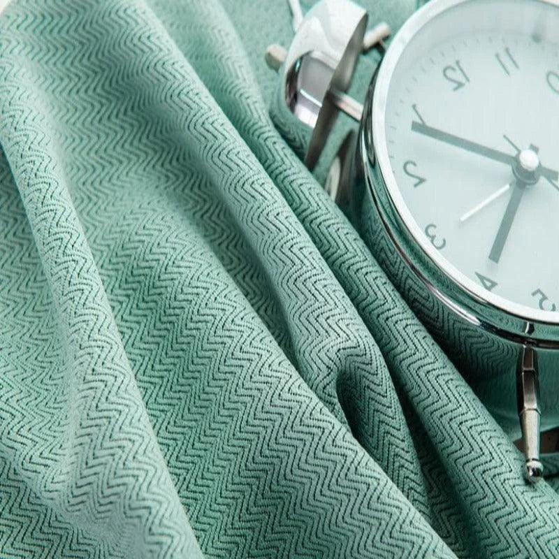 Montre réveil classique argentée posée sur un tissu vert avec motif à chevrons, mettant en valeur un design élégant et intemporel parfait pour la décoration de chambre ou bureau. Idéal pour ajouter une touche de sophistication à votre espace.