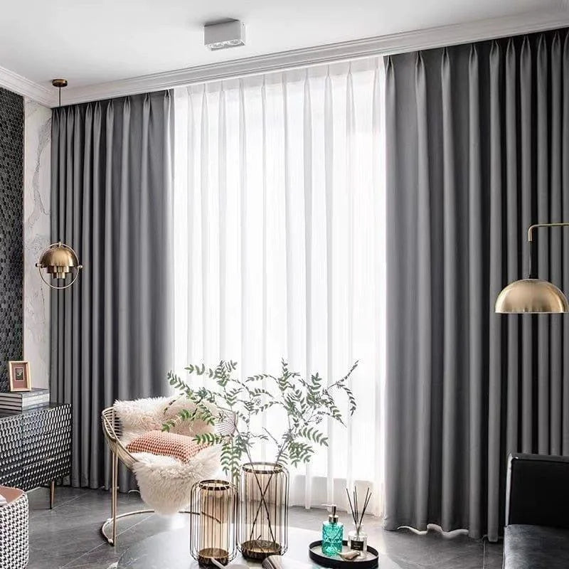 Rideaux élégants gris pour salon moderne, décoration intérieure chic avec mobilier tendance et accents dorés. Fenêtre habillée de doubles rideaux gris et voilages blancs pour un éclairage naturel optimal. Ambiance contemporaine avec fauteuil design, plantes d'intérieur et éléments décoratifs raffinés.