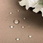 Gouttelettes d'eau sur une surface résistante, démontrant l'imperméabilité et la durabilité du tissu, avec des fleurs blanches en arrière-plan pour sublimer l'élégance du décor.