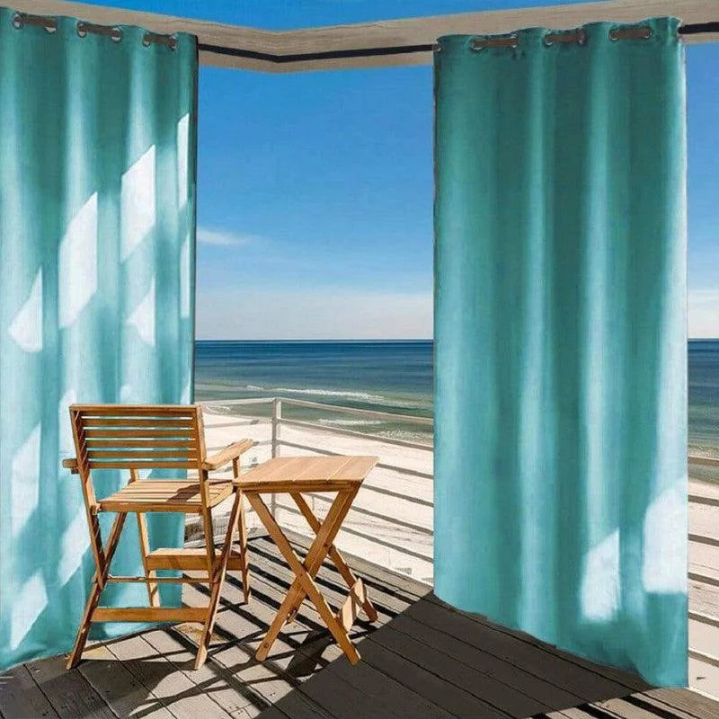 Rideaux extérieurs turquoise sur terrasse avec vue sur la mer, accompagnés de mobilier en bois pour un espace détente extérieur élégant et confortable, idéal pour profiter du soleil tout en se protégeant du vent.